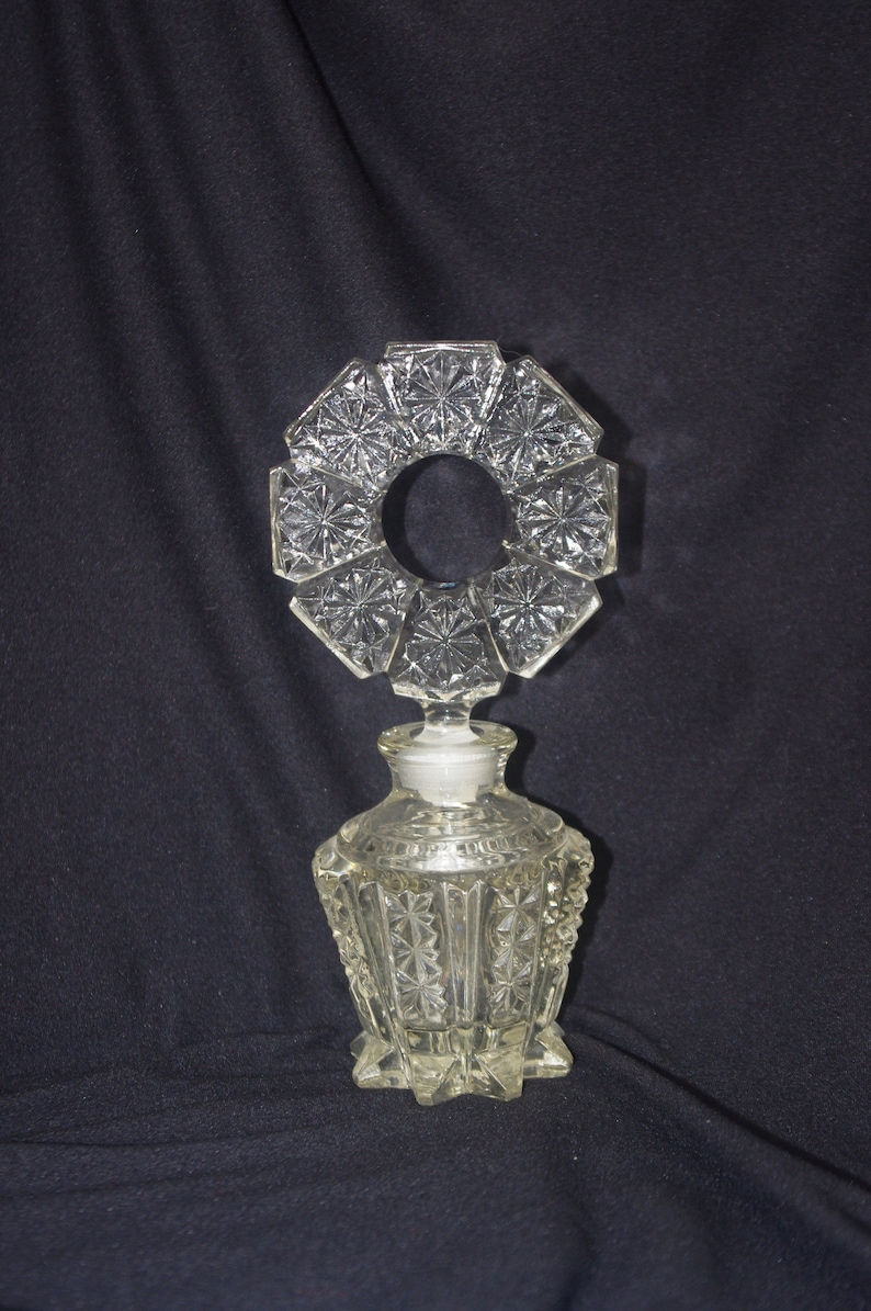 Pu&ograve; includere: Flacone di profumo in vetro trasparente con un design geometrico decorativo. La bottiglia ha un motivo a stella e un tappo circolare. La bottiglia &egrave; alta circa 13 cm.
