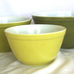 Può includere: Un set di tre ciotole da cucina impilabili in sfumature graduate di verde e giallo. Le ciotole presentano un esterno liscio a tinta unita con finitura lucida e un interno bianco a contrasto, caratterizzate da un design semplice e rotondo.