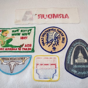 May include: A collection of vintage embroidered patches, including a Peter Pan design, a Native American scout emblem, and a Kansas Pacific Railway patch. The patches are in various shapes and colors, with text and detailed imagery.