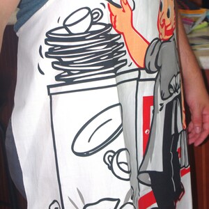 May include: White apron with a cartoon illustration of a chef and the words "King of the Kitchen" in red. The apron features a stack of plates, a cup, and a broken plate design.