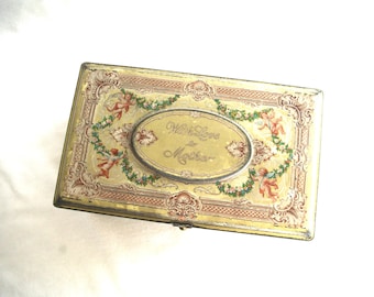 May include: Rectangular vintage tin box with a yellow background and ornate detailing. The box features an oval centerpiece with the words "With Love to Mother" and is decorated with cherubs and floral garlands.