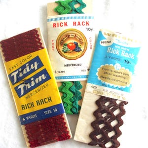 May include: Three vintage packages of rick rack trim in various colors. One package is yellow with red trim and the text "Tidy Trim." Another is white with green trim and the text "Rick Rack." The third is blue with brown trim and the text "Rick Rack."