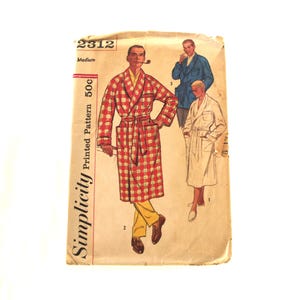 Puede incluir: Sobre de patrón Simplicity vintage con ilustraciones de batas de hombre. La imagen principal muestra a un hombre con una bata a cuadros rojos y blancos. El sobre está etiquetado como "2312 Medium" y "Printed Pattern 50c".