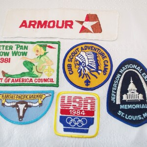 May include: A collection of vintage embroidered patches. Includes a white patch with "ARMOUR" in red, a Peter Pan patch, a Cub Scout Adventure Camp patch, a Kansas Pacific Railway patch, a USA 1984 Olympics patch, and a Jefferson National Expansion Memorial patch.