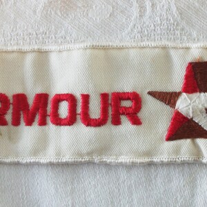 May include: Cream-colored embroidered patch with the word "ARMOUR" in red letters. A brown and red star design with a white star is on the right side of the patch. The patch has a white border.
