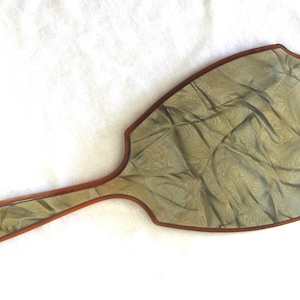 May include: An antique hand mirror with a decorative, patterned surface in shades of green and gold. The mirror has a wooden frame and handle with a dark brown finish. The overall shape is a paddle with a rounded top.