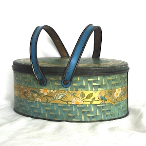May include: Vintage oval metal basket with a turquoise woven design and a gold band featuring floral and bird motifs. The basket has a blue handle and rim. A decorative piece, perfect for storage or display.