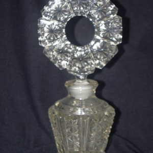 Pu&ograve; includere: Flacone di profumo in vetro trasparente con un tappo decorativo a forma di stella. La bottiglia ha un design geometrico sfaccettato. Il tappo &egrave; di forma circolare con un'apertura centrale. La bottiglia &egrave; alta circa 15 cm.