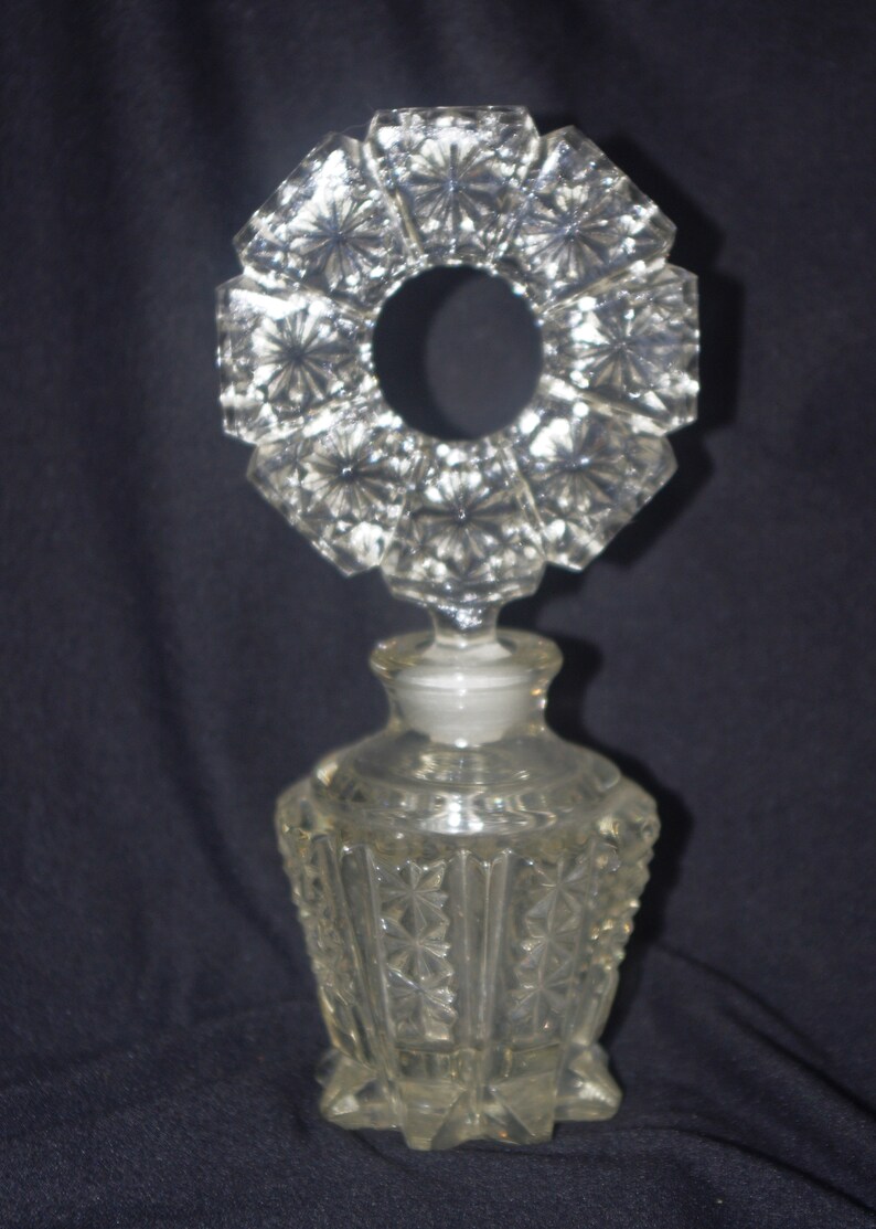 Pu&ograve; includere: Flacone di profumo in vetro trasparente con un tappo decorativo a forma di stella. La bottiglia ha un design geometrico sfaccettato. Il tappo &egrave; di forma circolare con un'apertura centrale. La bottiglia &egrave; alta circa 15 cm.