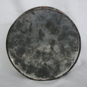 May include: A round, metal tray with a distressed, mottled gray surface. The tray's edge is a darker gray with a thin, colorful border. The tray appears to be vintage or antique.