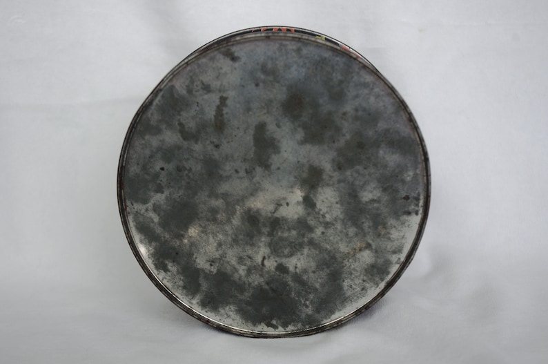 May include: A round, metal tray with a distressed, mottled gray surface. The tray's edge is a darker gray with a thin, colorful border. The tray appears to be vintage or antique.
