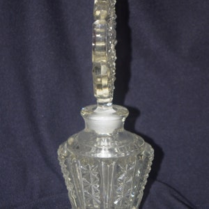 Pu&ograve; includere: Flacone di profumo in vetro trasparente con tappo decorativo. La bottiglia ha un design a stella sfaccettato sul corpo e un tappo alto e ornato. La bottiglia &egrave; probabilmente vintage e aggiunge un tocco di eleganza.