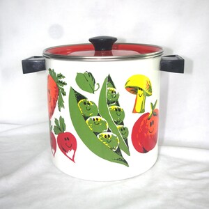 May include: A white enamel stockpot with a red lid and black handles. The exterior features a colorful graphic print of smiling vegetables, including green pea pods, a yellow mushroom, a red tomato, and red radishes with green leafy tops.