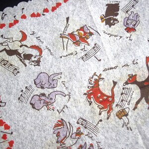 May include: A vintage, off-white handkerchief with a scalloped edge. It features whimsical illustrations of animals, musical notes, and hearts in brown, red, and purple. Text includes phrases like "I love you" and "Je t'aime."
