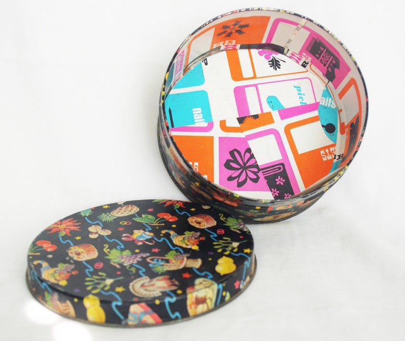 May include: A vintage round tin box with a lid. The lid is black with colorful illustrations. The interior of the box is white with a colorful geometric pattern. The box is open, revealing the interior design.