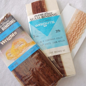 Könnte beinhalten: Drei Packungen Flexi-Lace Seam Binding von Wrights. Eine Packung ist braun, mit dem Text "Seal Brown 92". Die anderen beiden Packungen sind braun und beige. Die beige Packung hat einen gewellten Rand. Die Packungen liegen auf einer weißen Oberfläche.