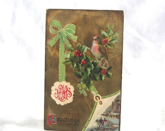 May include: Antique Christmas postcard with a robin on holly and red berries. A green bow and the word "Greetings" are present. The postcard has a gold background and a winter scene in the corner.