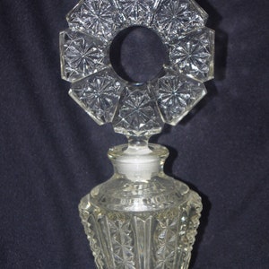 Pu&ograve; includere: Flacone di profumo in vetro trasparente con un design geometrico decorativo. Il flacone ha una base e un corpo sfaccettati, un tappo e una parte superiore unica a forma di alone ottagonale. Il flacone &egrave; alto circa 15 cm.