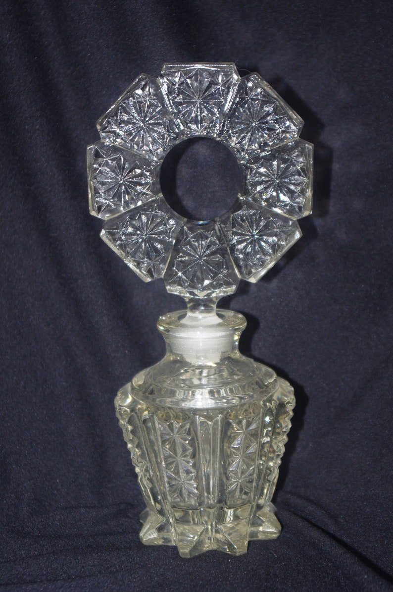 Pu&ograve; includere: Flacone di profumo in vetro trasparente con un design geometrico decorativo. Il flacone ha una base e un corpo sfaccettati, un tappo e una parte superiore unica a forma di alone ottagonale. Il flacone &egrave; alto circa 15 cm.