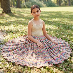 May include: A sleeveless dress featuring a cream-coloured crocheted bodice with thin straps and a wide, flared skirt made of multicoloured yarn in a chevron pattern. The skirt displays a vibrant gradient of pastel hues and a scalloped hemline.