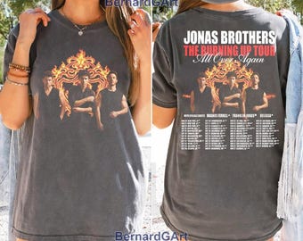 Op de afbeelding: Een antracietgrijs T-shirt met korte mouwen en een afbeelding van de Jonas Brothers voor een vlammenontwerp. De achterkant toont de tekst Jonas Brothers The Burning Up Tour All Over Again met een lijst van tourdata en locaties.