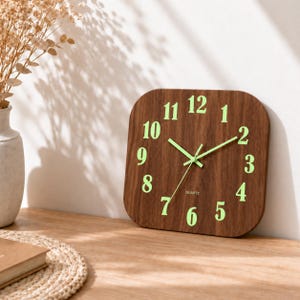 May include: A square wall clock with a dark brown wood grain finish, featuring large, luminous light green numerals from 1 to 12. The clock has matching light green hour, minute, and second hands, with the word QUARTZ printed in small white letters.