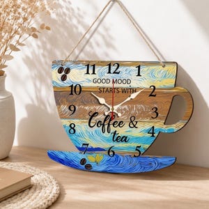 May include: A wall clock shaped like a coffee cup with a hanging twine cord. The clock face features a swirling blue, yellow, and brown painted pattern with black numbers 1 through 12. Text reads: GOOD MOOD STARTS WITH Coffee & tea.