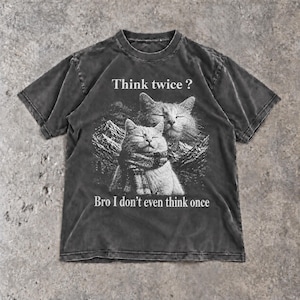 Könnte beinhalten: Ein anthrazitfarbenes Kurzarm-T-Shirt mit einer Grafik von zwei Katzen, von denen eine einen Schal trägt, vor einer Berglandschaft. Der Text "Think twice ?" steht über den Katzen und "Bro I don't even think once" ist unter der Grafik gedruckt.