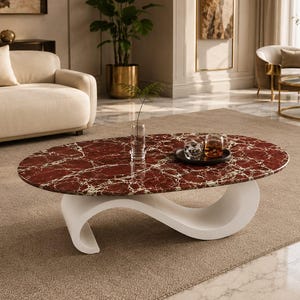 Op de afbeelding: Een ovale salontafel met een dieprood marmeren blad met witte aders en een gladde, witte, golfvormige voet. Op het tafeloppervlak staan een heldere glazen vaas, een klein zwart dienblad, een glazen beker en een mok met een donkere vloeistof.