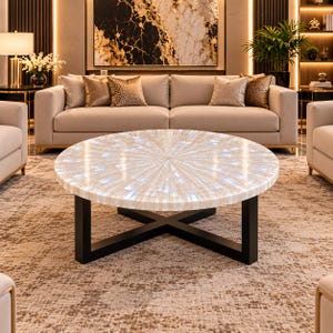 May include: A round coffee table featuring a white, iridescent, sunburst-patterned tabletop surface made of inlaid material. The table is supported by a sturdy, black, cross-shaped metal base that provides a stable foundation for the top.