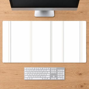 May include: A rectangular desk mat featuring a clean white surface accented by thin, vertical light gray stripes. The mat is positioned on a wooden surface below a computer monitor and a white wireless keyboard, providing a wide workspace area.