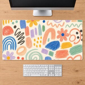 May include: A rectangular desk mat featuring a cream-colored background with a repeating pattern of colorful crayon-style drawings. The design includes various shapes such as flowers, rainbows, swirls, dots, and abstract blocks in blue, orange, yellow, green, and purple.
