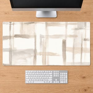 Puede incluir: Una alfombrilla de escritorio rectangular con un patrón abstracto de pinceladas horizontales y verticales superpuestas en tonos beige, crema y gris claro. El diseño crea un efecto de cuadrícula en la superficie, ofreciendo un fondo neutro.