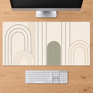May include: A rectangular desk mat featuring a cream-colored background with a series of thin vertical lines and arched shapes in shades of sage green, tan, and dark brown. The mat is positioned beneath a computer monitor and a white keyboard.