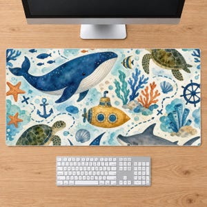 Peut inclure: Un tapis de bureau rectangulaire présentant une illustration à l'aquarelle d'une scène sous-marine avec une grande baleine bleue, un sous-marin jaune, deux tortues marines, un requin, des étoiles de mer orange, du corail bleu et des coquillages.