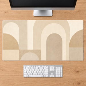 May include: A rectangular desk mat featuring a geometric pattern of overlapping arches and semi-circles in various shades of beige, cream, and tan. The design consists of smooth, solid color blocks arranged in a repeating, layered composition.