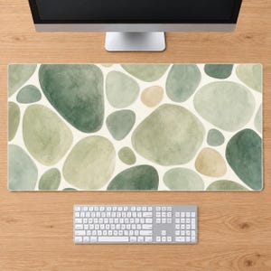 May include: A rectangular desk mat featuring a repeating pattern of watercolor-style organic shapes in various shades of sage green, forest green, and soft beige. The mat is positioned on a wooden surface beneath a computer monitor and keyboard.
