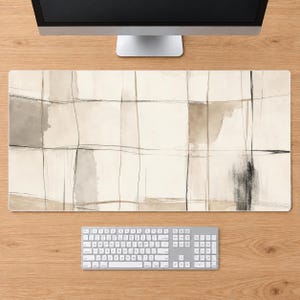 May include: A rectangular desk mat featuring an abstract design with a cream-colored background, layered with soft beige and gray watercolor-style washes, and accented by thin, intersecting black lines that create a grid-like pattern.