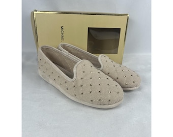May include: A pair of beige quilted slip-on shoes featuring small gold-tone studs at each intersection of the diamond pattern. The shoes are positioned in front of a tan cardboard box with the word MICHAEL printed on the side.