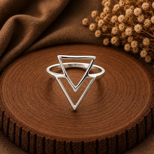 May include: A silver ring featuring a geometric design composed of two stacked, open-frame triangles. The metal has a polished, reflective finish, and the band is thin and circular, supporting the prominent triangular structure on the front.