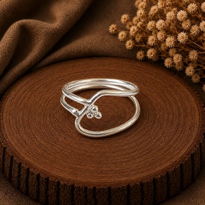 May include: A silver ring featuring a double band design that curves to meet at a central point. The focal point of the ring is a cluster of three small, polished silver spheres arranged in a triangular formation at the intersection of the bands.