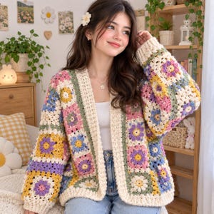 May include: A long-sleeved cardigan made of crocheted granny squares in pastel shades of pink, yellow, blue, and purple, featuring a cream-coloured border and cuffs. The garment is worn over a white top and blue denim jeans, with a flower hair clip.