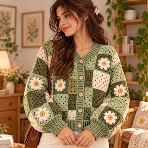 May include: A long-sleeve crochet cardigan featuring a patchwork design of alternating dark green, light green, and cream-coloured squares. Several squares are decorated with white daisy motifs with yellow centres. The cardigan has a V-neck and buttons.