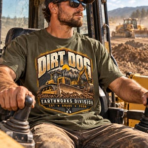 Peut inclure: Un t-shirt vert olive avec une impression graphique représentant des engins de chantier jaunes, des montagnes et le texte DIRT DOG EARTHWORKS DIVISION CUT GRADE PUSH avec deux pelles croisées. Le motif est centré sur la poitrine.