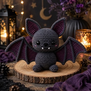 May include: A crocheted bat plush toy with a dark gray body, large pointed ears with purple inner sections, and wide wings featuring purple accents. The bat has two black plastic eyes, a small black nose, and two white fangs protruding.