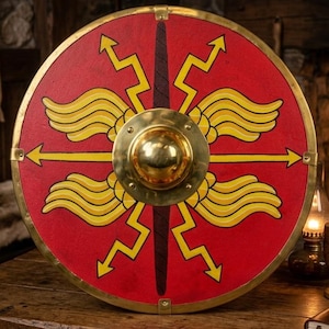 May include: A circular red wooden shield featuring a central brass boss, a dark vertical stripe, and yellow painted designs of four stylized wings and four lightning bolts pointing outward toward the brass-trimmed outer edge.