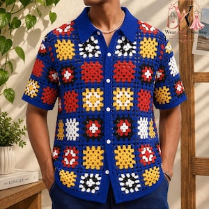 Pode incluir: Uma camisa de manga curta com botões, apresentando um padrão de quadrados de crochê em azul com detalhes alternados de quadrados vermelhos, amarelos, brancos e pretos. A camisa tem um colarinho clássico e fecho frontal de botões em malha aberta.