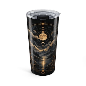 May include: A black cylindrical tumbler with a clear plastic lid featuring a gold and dark blue illustration of a moon, celestial phases, and a mountain landscape reflected in a lake, framed by decorative botanical elements and stars.