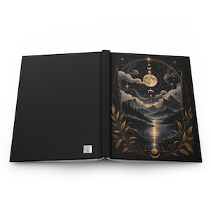 May include: An open hardcover journal with a solid black back cover and a front cover featuring a gold and dark blue illustration of a moonlit mountain landscape, a lake, and celestial phases framed by golden laurel branches and stars.
