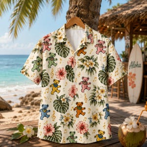 Peut inclure: Une chemise à manches courtes boutonnée de couleur crème avec un motif répétitif d'ours dansants en rose, vert, jaune et bleu, entremêlés de fleurs d'hibiscus tropicales, de feuilles de monstera vertes et de petites notes de musique dorées.